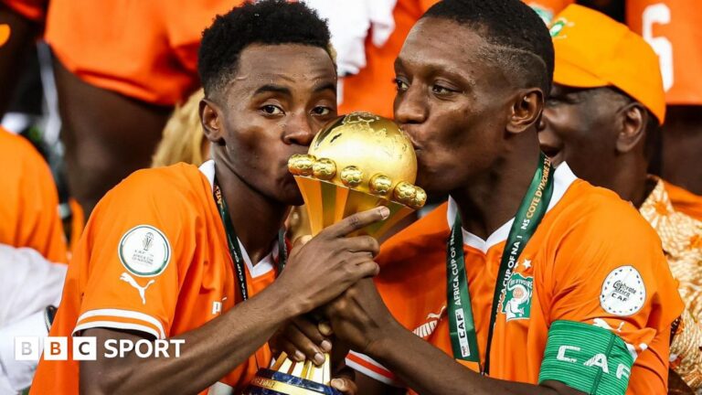 Africa Cup of Nations to be held every four years from 2028 Simon Adingra and Max-Alain Gradel seen from chest up, both wearing bright orange Ivory Coast football shirts with medals around their necks, hold the golden Africa Cup of Nations trophy between them and kiss the top of it. Adingra is looking directly into the camera while Gradel casts his eyes to the left of the screen
