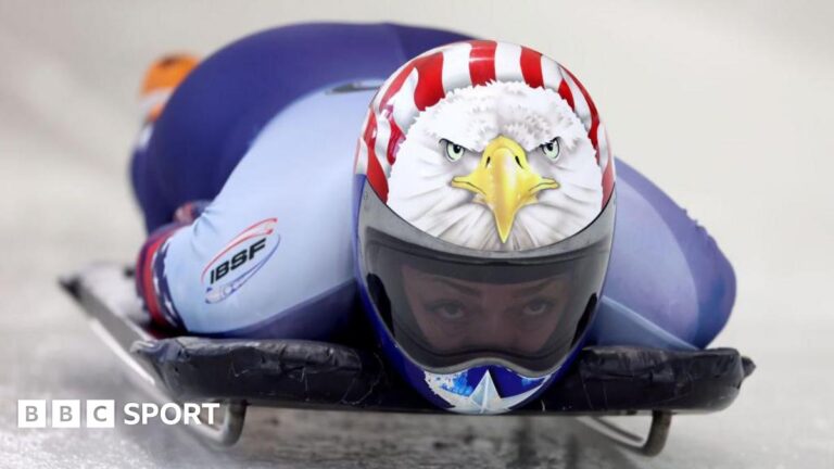 Winter Olympics: Canada skeleton chiefs cleared in qualifying row Katie Uhlaender competing the women’s skeleton World Championships in 2025. She is wearing a crash helmet which is painted with an image of an American eagle and the stars and stripes of the USA flag. Her eyes can be seen through a clear visor.