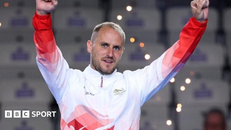 Commonwealth Games 2026: Sam Tolchard joy at bowls gold for England Sam Tolchard, wearing a white and red England tracksuit top, raises his arms while standing on the podium at the 2026 Commonwealth Games in Glasgow