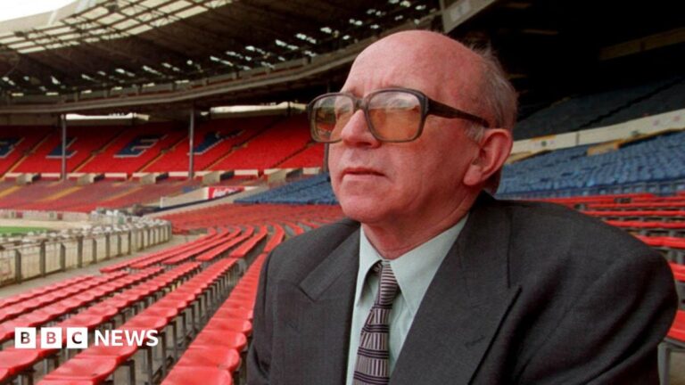 Heading footballs caused Nobby Stiles’ brain disease, coroner finds Catherine Turnbull is smiling at the camera. She is wearing a pale blue t-shirt and dark framed glasses. Catherine has short light brown hair. She has some bushes behind her with are slightly out of focus.
